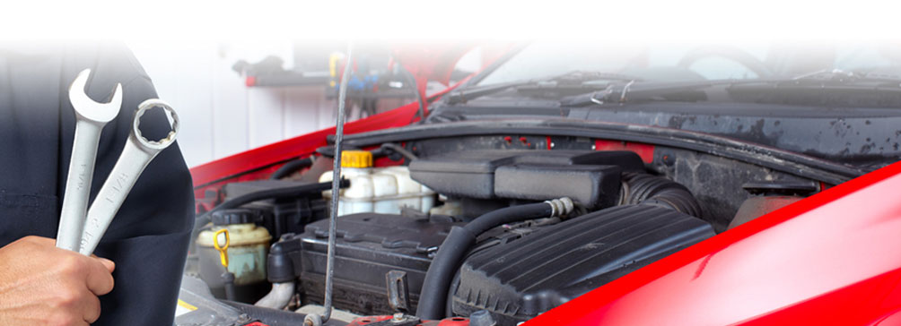 Man holding wrenches in front of an open car hood